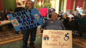 Tom Osborn and Mike Mayer holding up signs that say "Don't Roll Back Our Rights" and " Disability Rights are Human Rights" during Rally Day 2017