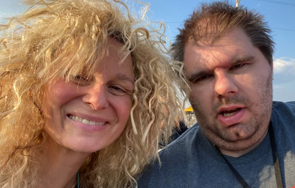 Jenny wears a blonde Tina Turner wig and poses with Bobby, both smiling for a picture