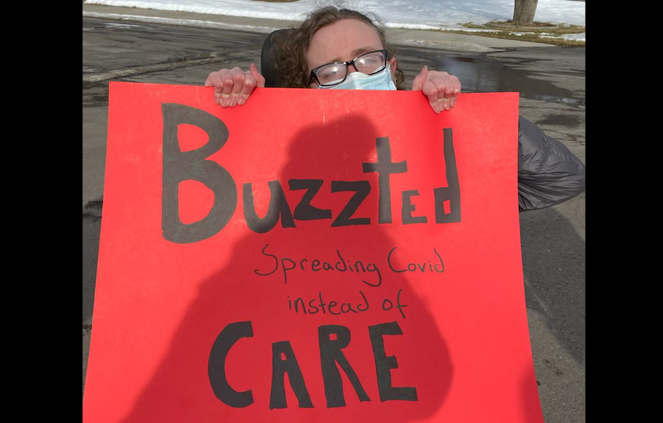 Maddy holds a sign saying "Buzzted spreading COVID instead of care"
