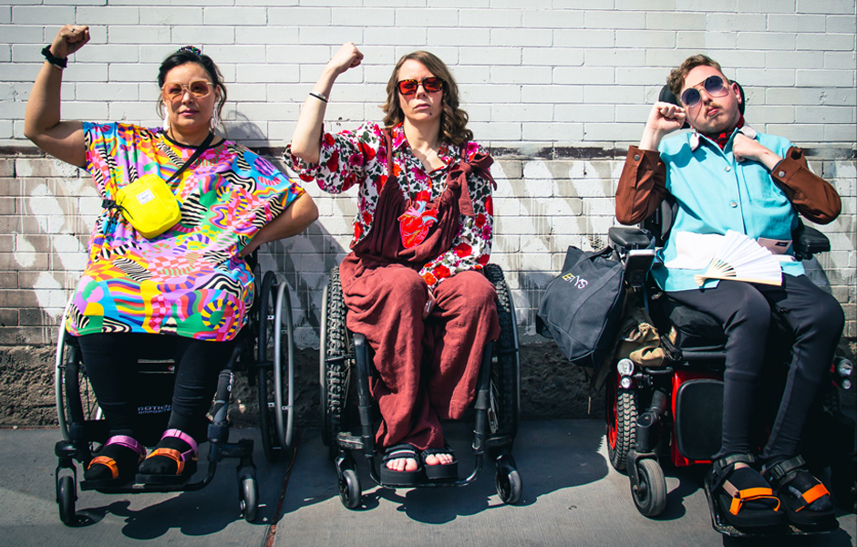 Three individuals dressed in incredible clothing from Betty's pose with their fists raised up in power