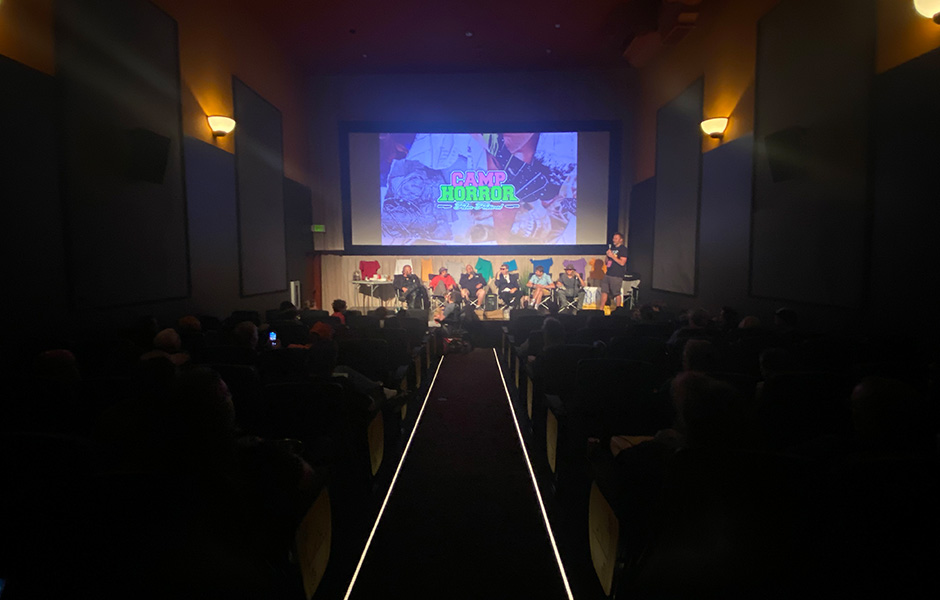 An image taken from the back of the Roxy theater, with the audience in the dark on the sides of the image, and the Camp Horror creators lit up on stage