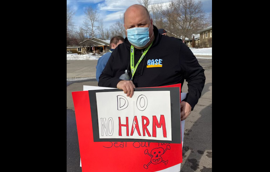 Jason holds a sign saying "Do no harm"