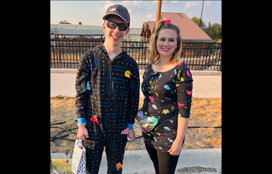 Christian, dressed up in a Pac-Man onesie poses with Madison, who wears a black dress with paint splashes