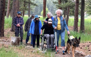 Six people traveling along the Rock Creek confluence trail, the lead person is using a white cane and has a guide dog, the second person is using the manual wheelchair, and the rest are ambulatory