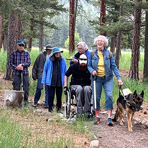 Six people traveling along the Rock Creek confluence trail, the lead person is using a white cane and has a guide dog, the second person is using the manual wheelchair, and the rest are ambulatory