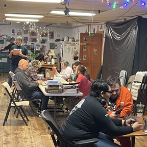BASE participants collaborate on small projects at art group, surrounded by tools and supplies beneath colorful string lights; the mood is focused and friendly.